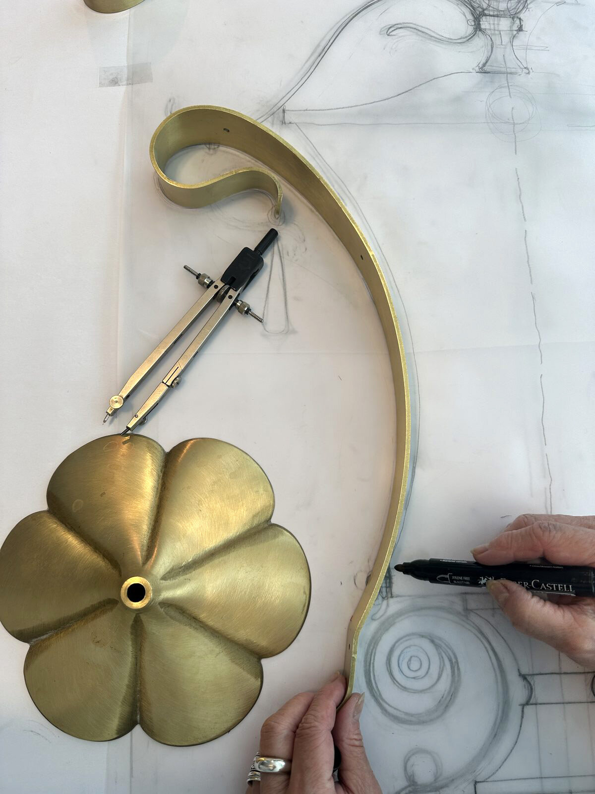 Brass volute and corolla placed over the technical drawing, with a compass beside them