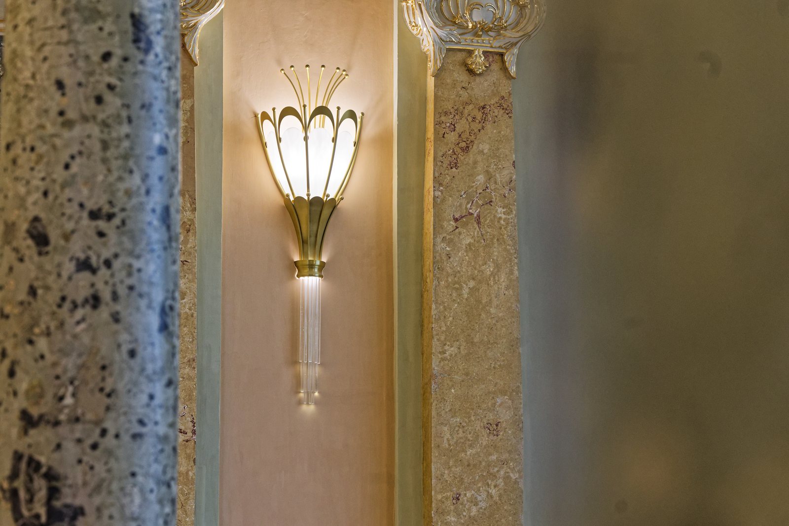 A lit Art Nouveau wall sconce, mounted between two marble columns