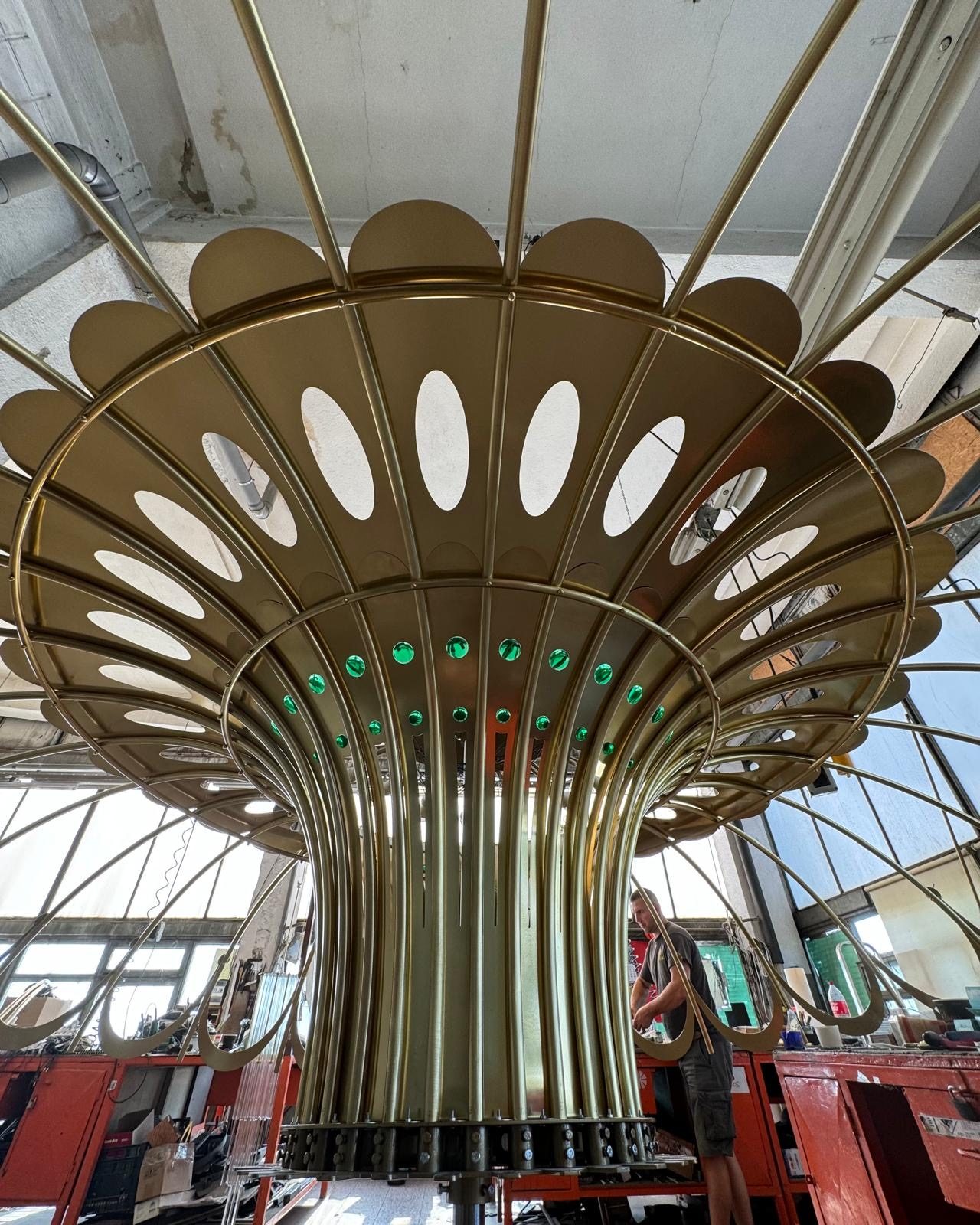 The large brass chandelier seen from below, with curved ribs and green glass droplets