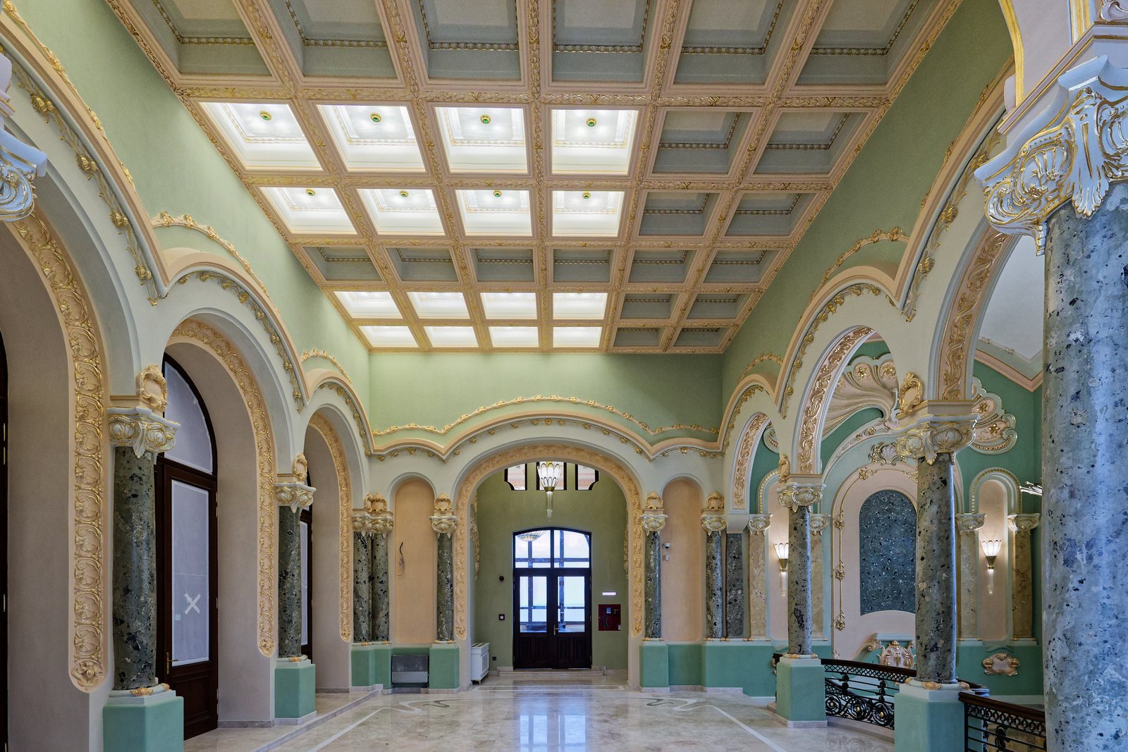 A hall with a lit coffered ceiling, marble columns and green walls, in the Constanța Casino