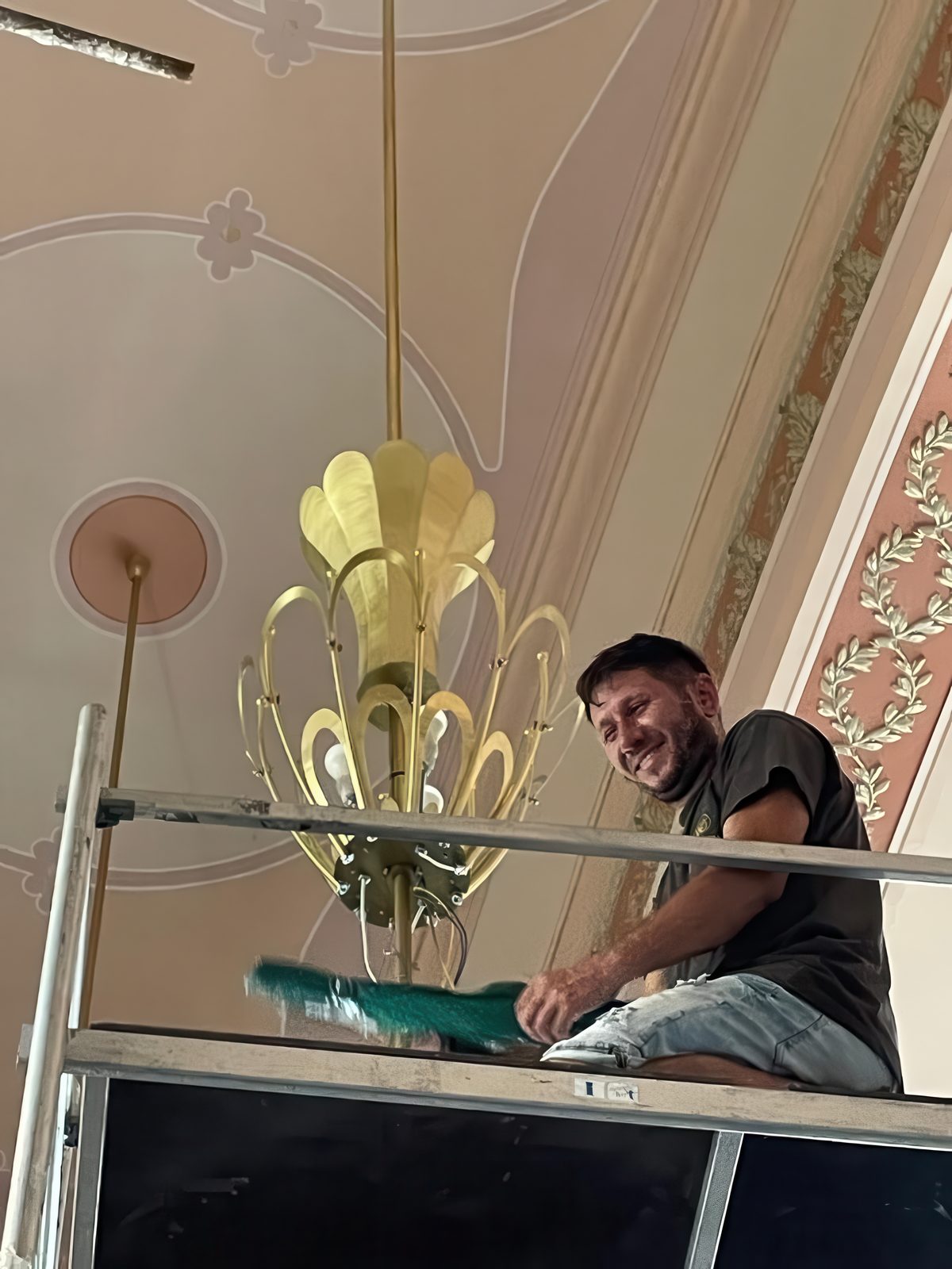 A craftsman on scaffolding beside a chandelier, beneath the painted ceiling of the Casino