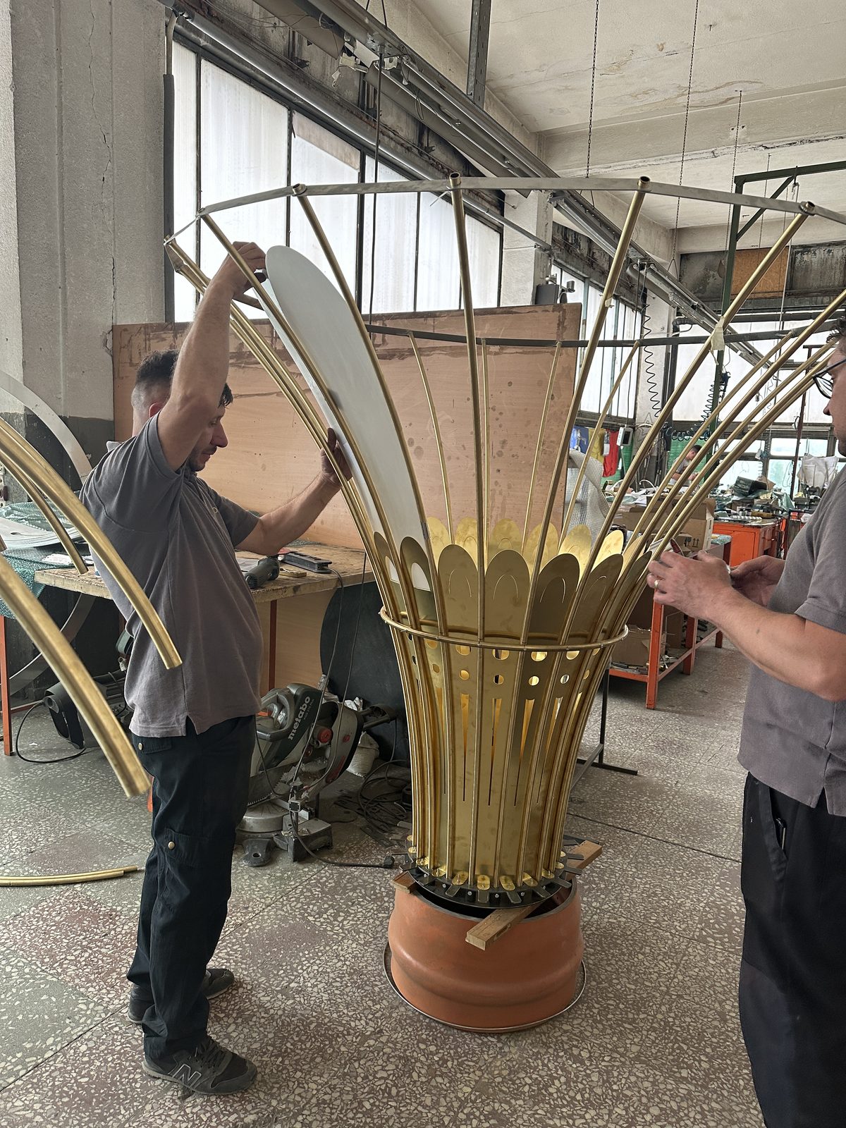 Two craftsmen mounting petals on the corolla of a brass chandelier