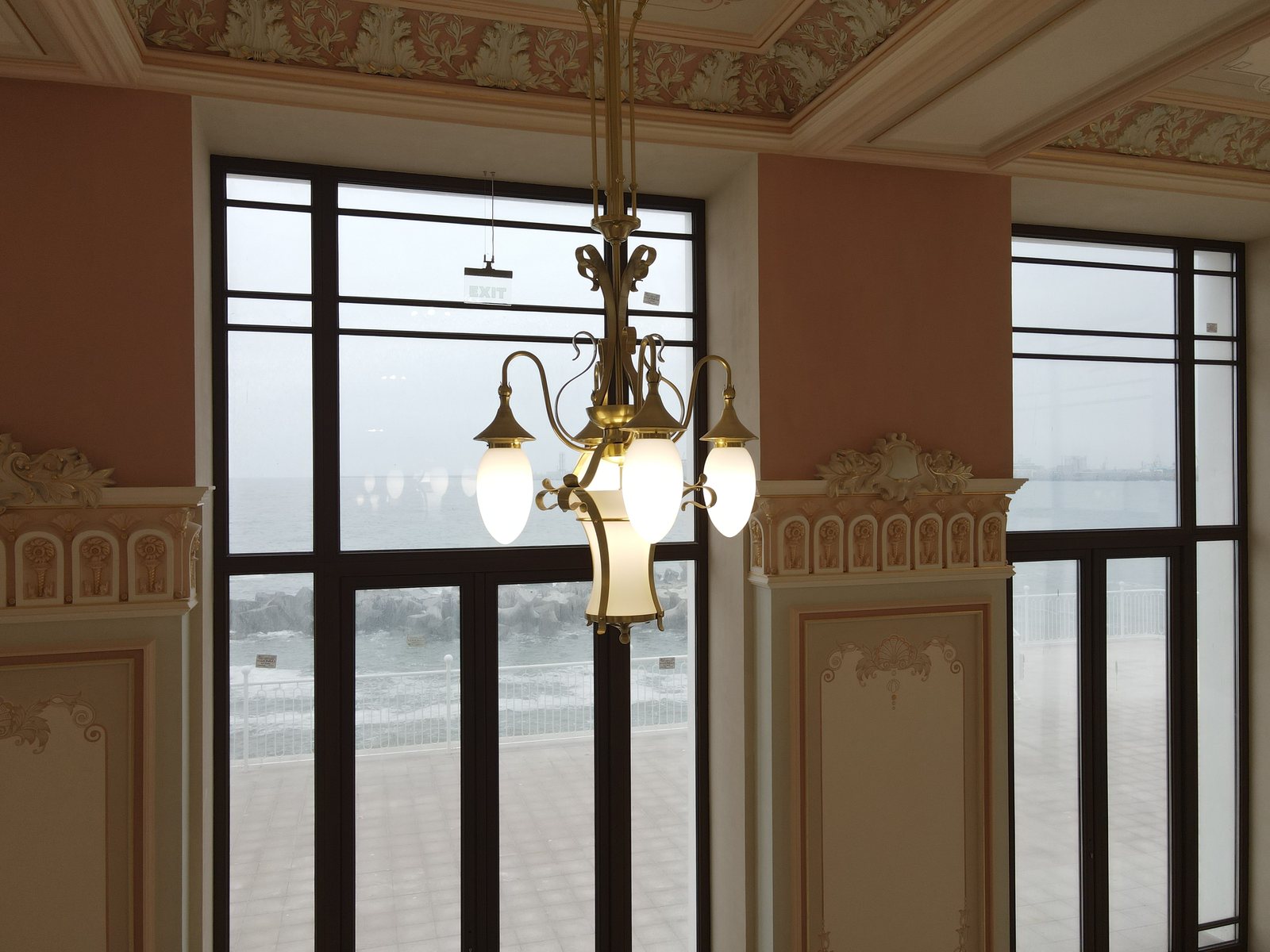 A brass pendant with three opal glass globes in front of a large window looking out to sea