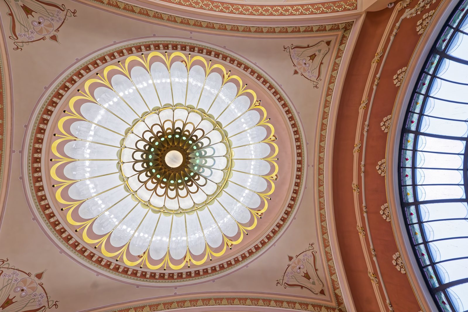A large circular ceiling light in opal glass and brass, seen from below, against the painted ceiling