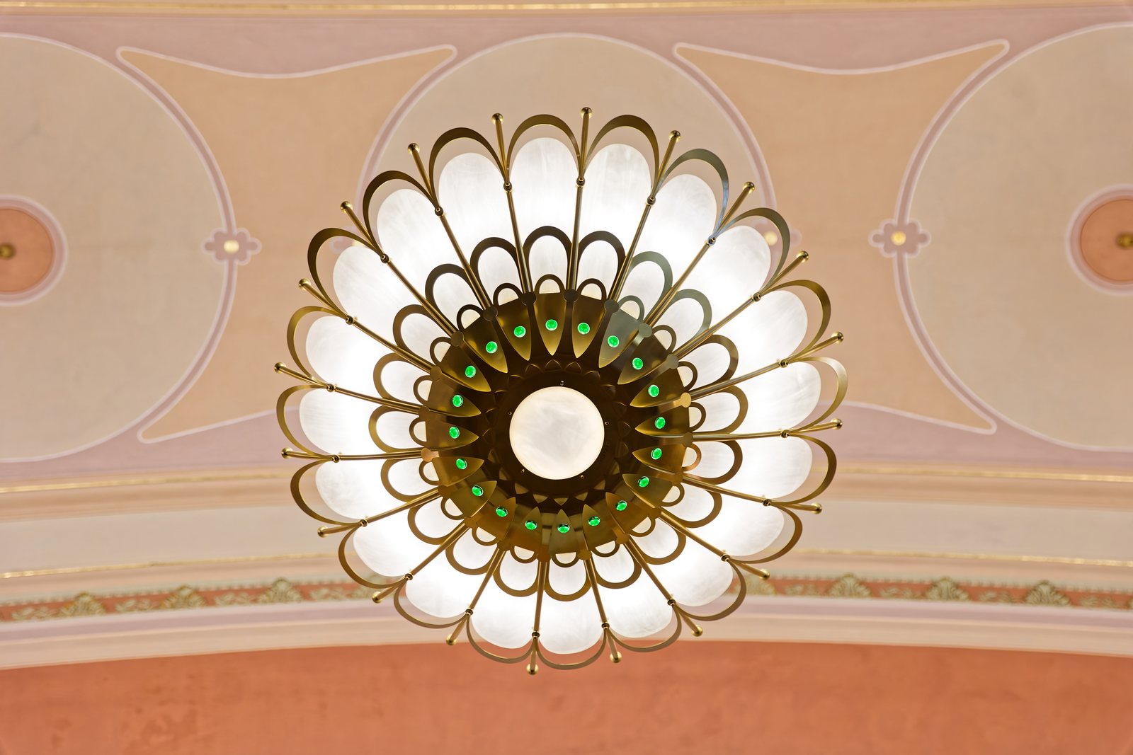 A round ceiling light with opal glass petals and green glass droplets, against a painted ceiling