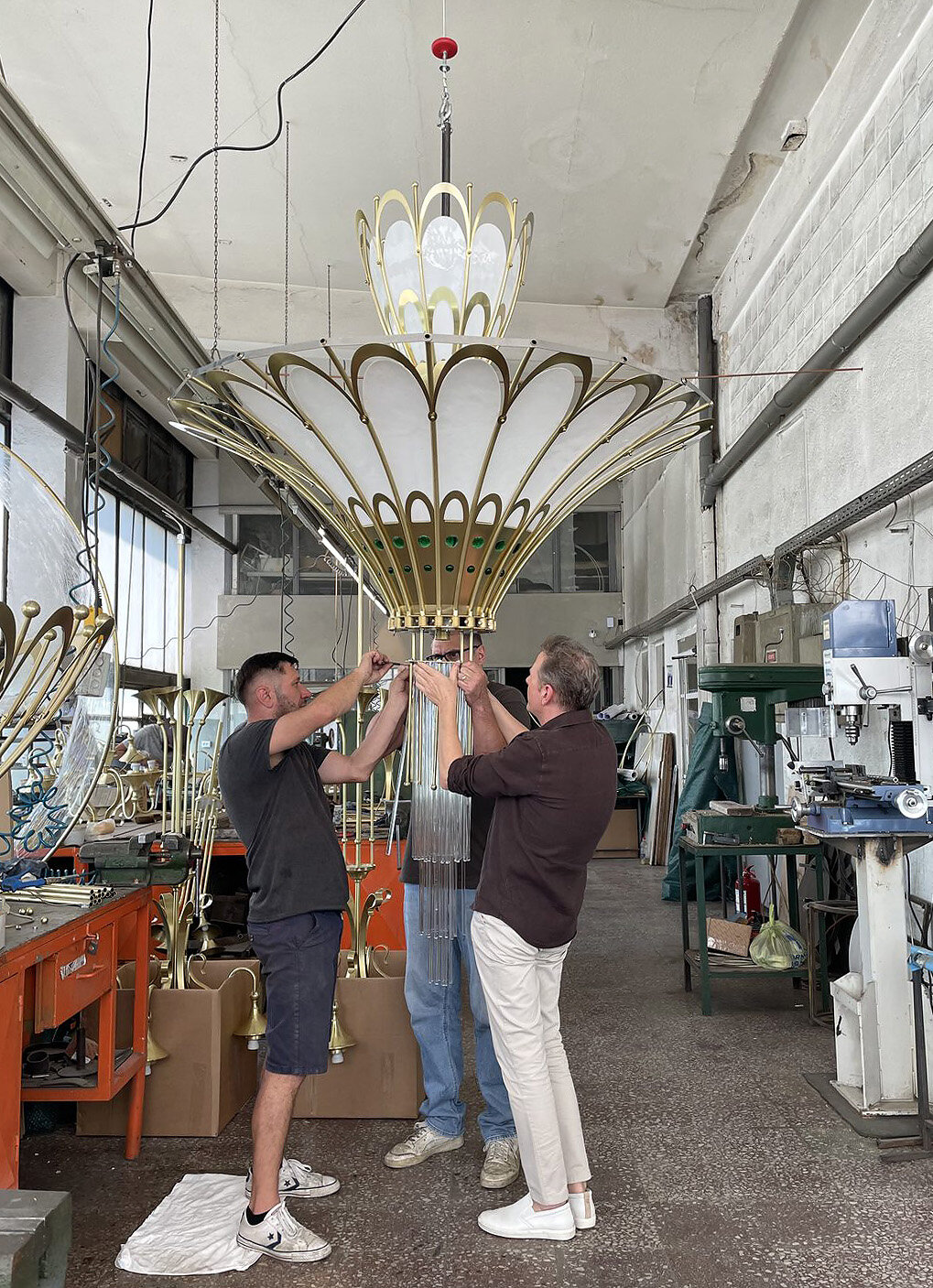 A chandelier lit for the first time, suspended in the workshop, with the team below