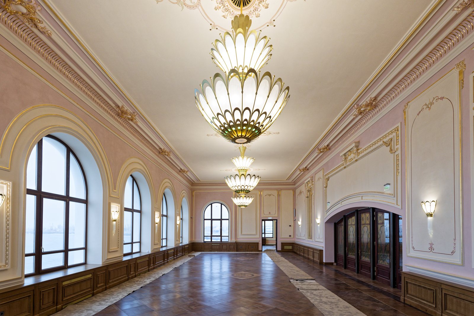 A long salon with arched windows and lit Art Nouveau chandeliers with opal glass petals