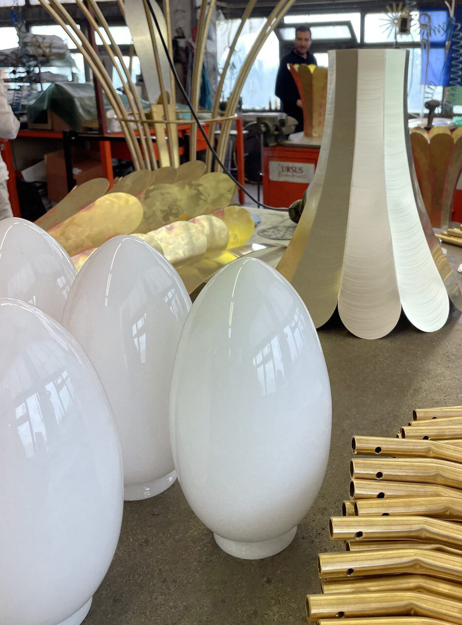 Egg-shaped opal glass globes next to a brass corolla with petals, in the workshop
