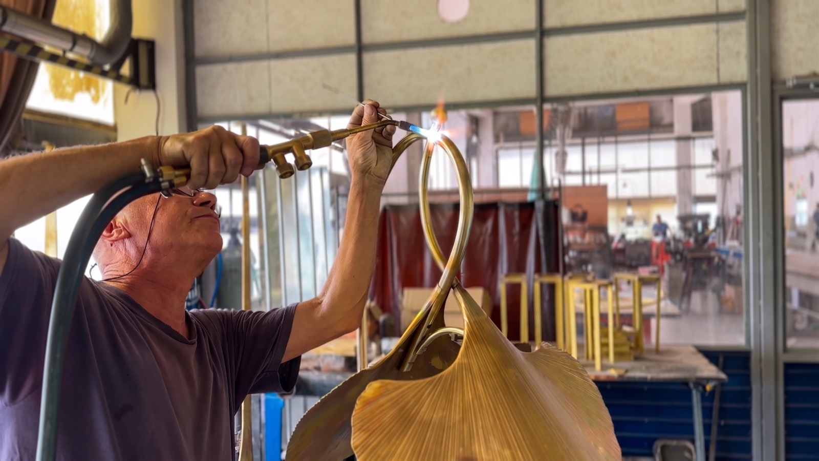 Craftsman flame-brazing the curved brass elements of a contemporary light fixture