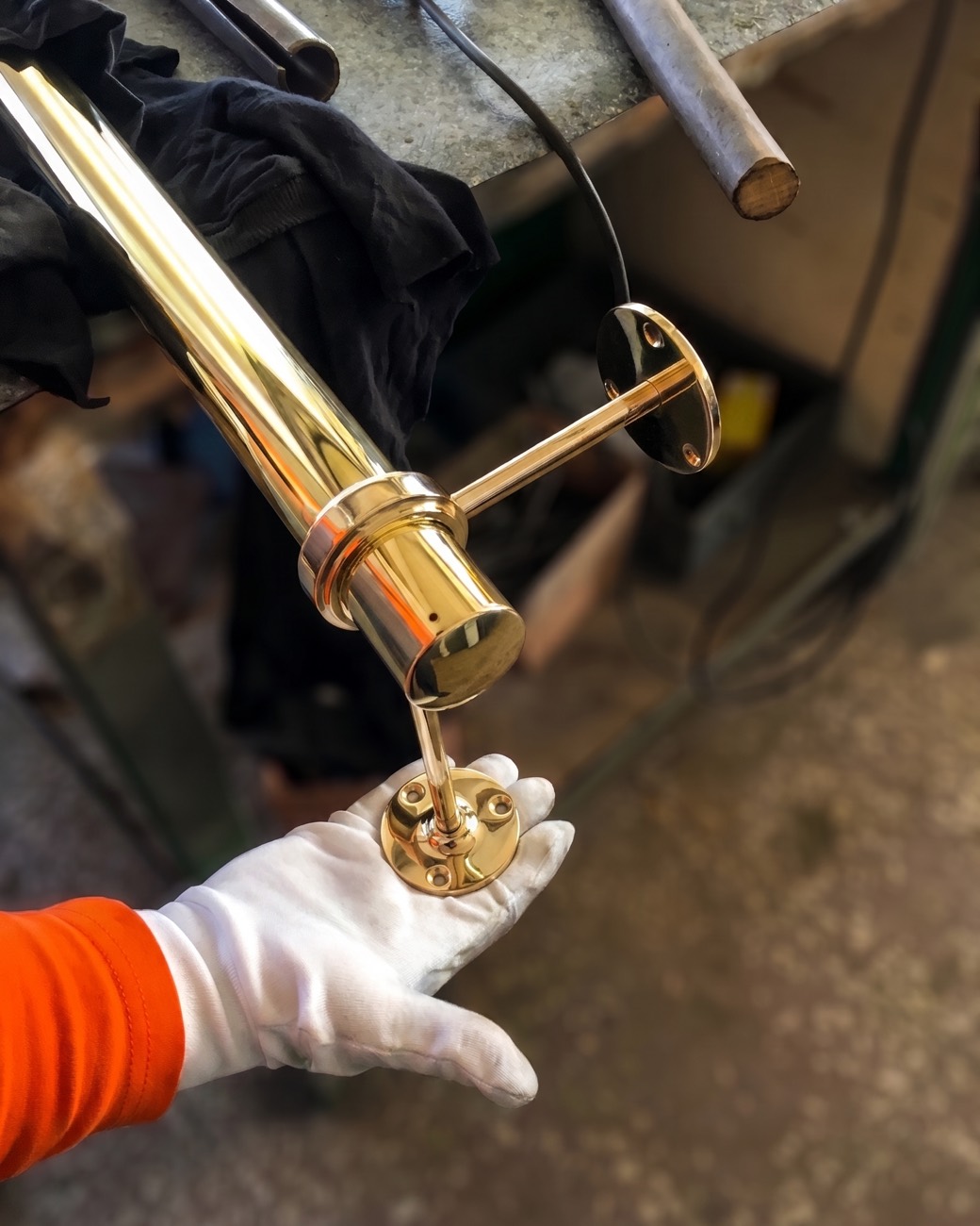 White-gloved hand presenting a mirror-polished brass sconce