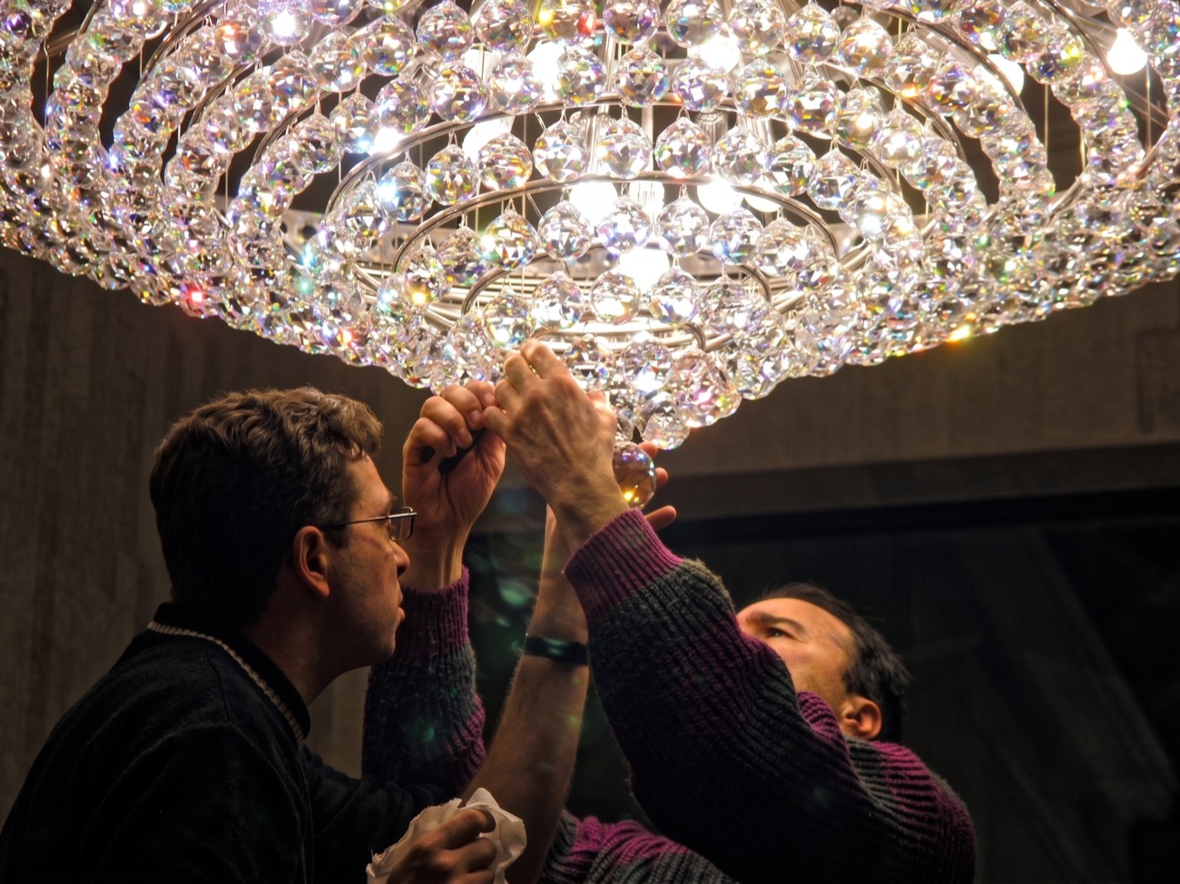 Two craftsmen mounting the crystal spheres of a lit chandelier