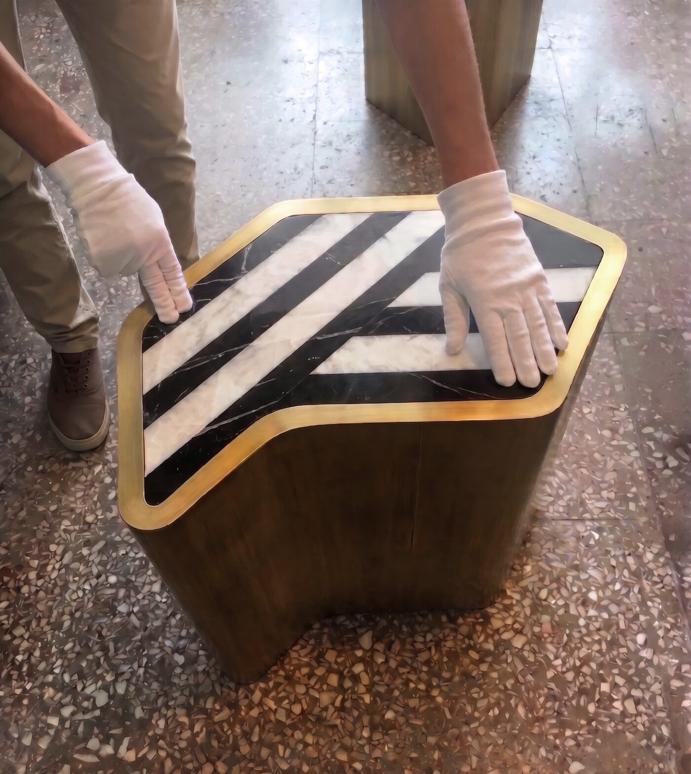 Side table with black-and-white marble top and patinated brass body, placed with white gloves