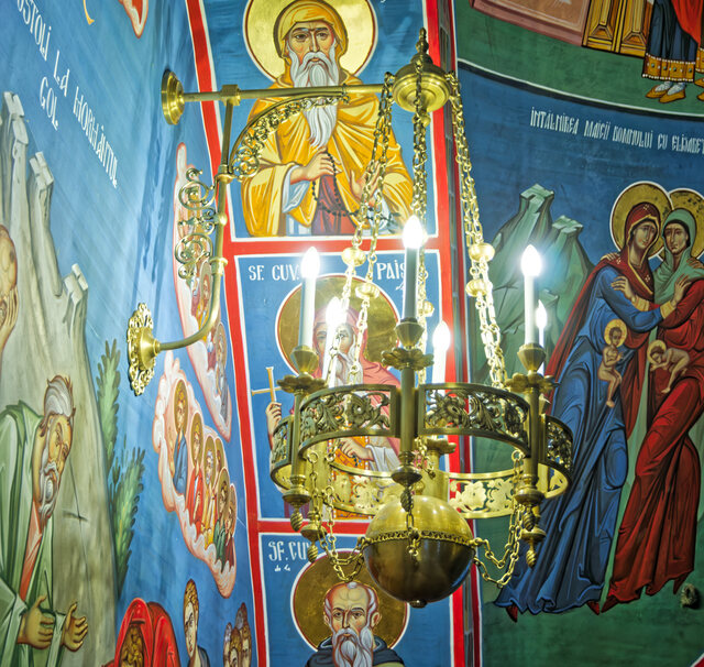 A brass bracket sconce with six arms and a sphere at its base, fixed to the painted wall of the church in Săpânța