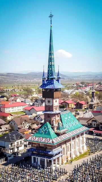 The church in Săpânța seen from above, its tower roofed in coloured tiles and the blue crosses of the Merry Cemetery around it