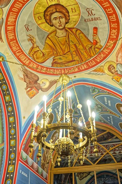 A brass chandelier with six arms, against the painted vault of the church in Săpânța