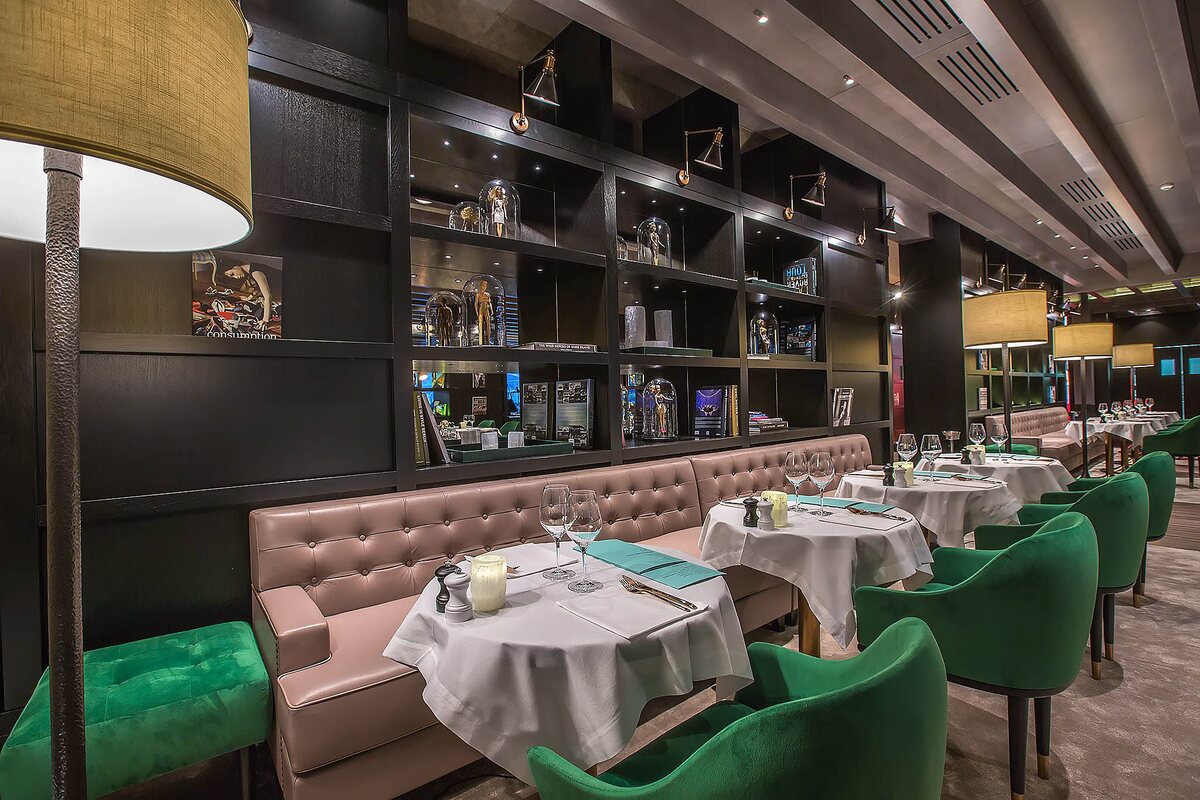 The restaurant at Stejarii Country Club: the black library wall with the FD.STIL reflector wall lights on brass arms, and a floor lamp with a brass shade in the foreground