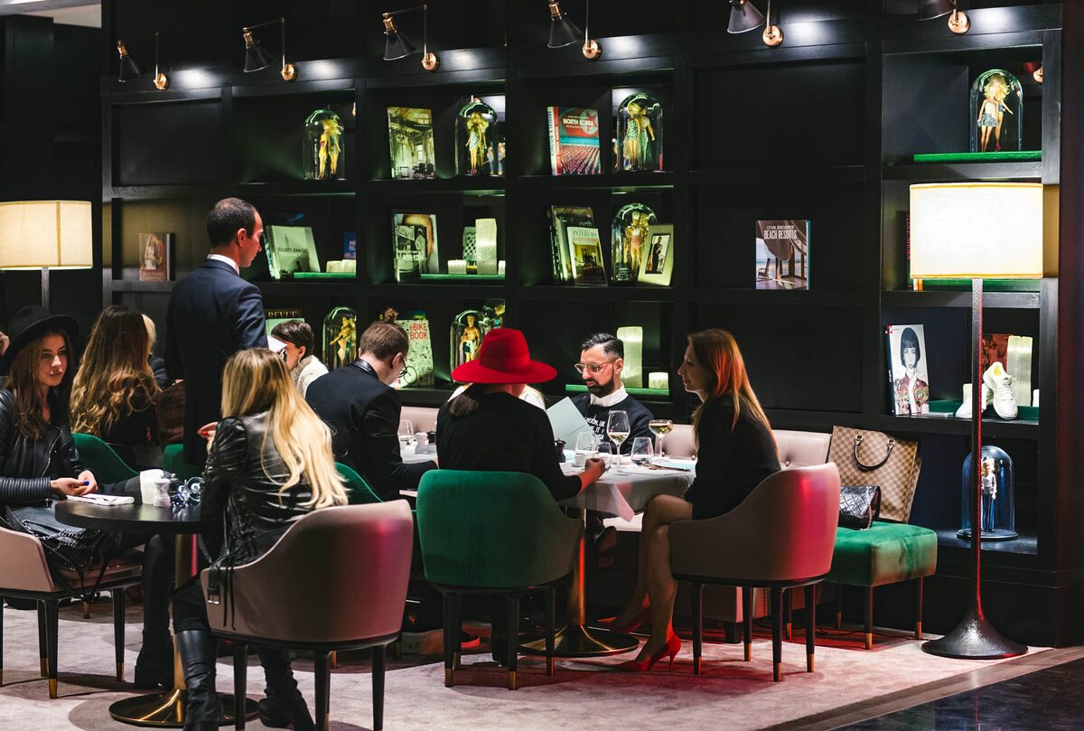 The restaurant at Stejarii Country Club full of guests in the evening, lit by the reflector wall lights on the library and the floor lamps between the tables